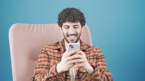 Happy-young-handsome-man-sitting-on-sofa-using-online-mobile-apps.